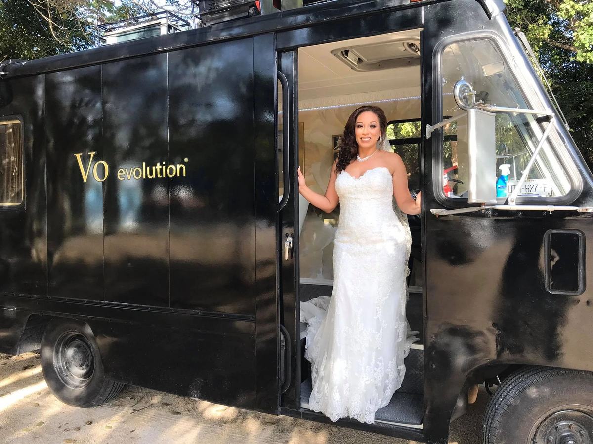 A bride in her gown standing at the open door of the Beauty Truck